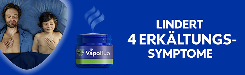 Vater und Sohn liegen zufrieden schlafend im Bett. Ihre Brust wurde jeweils mit WICK VapoRub Erkältungssalbe eingerieben, Dämpfe steigen auf. Der Text dazu sagt: Lindert vier Erkältungssymptome.